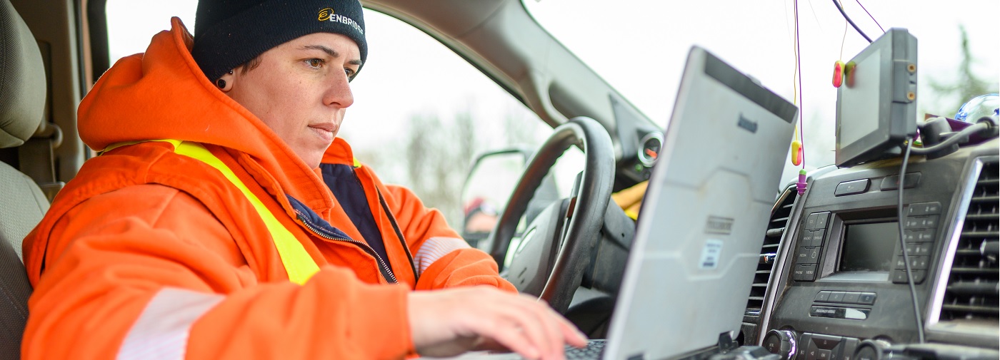 Worker in orange jacket working on laptop in vehicle