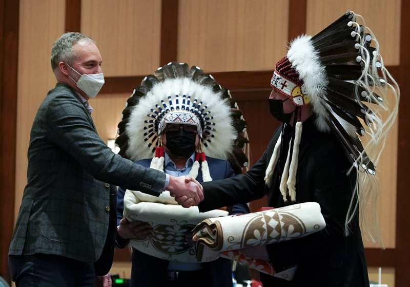 Man in a suit shaking hands with a chief wearing headdress