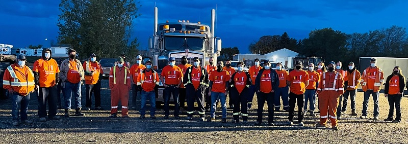 Large group in front of a semi trailer, all wearing orange shirts