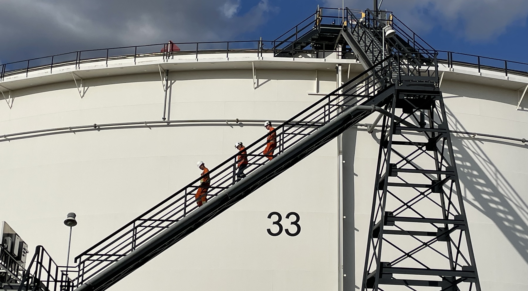 Three workers walking down a tank ladder