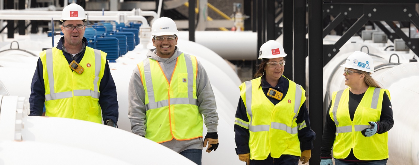Four people in helmets and safety vests among white pipes