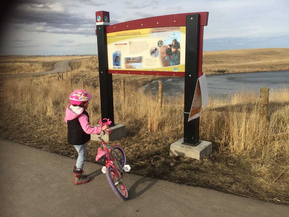 Child riding bike in front of nature trail sign