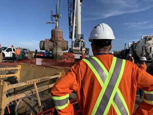 Worker watching crane lift old pipe valve