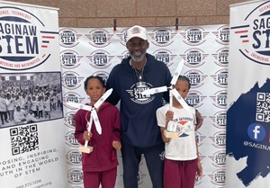 Adult with two kids in front of a banner stand