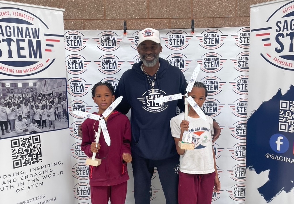 Adult with two kids in front of a banner stand