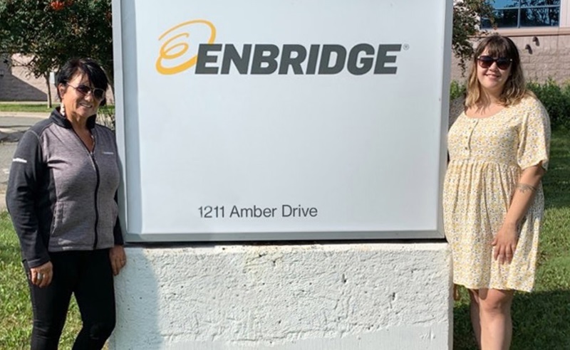 Two women standing beside a sign