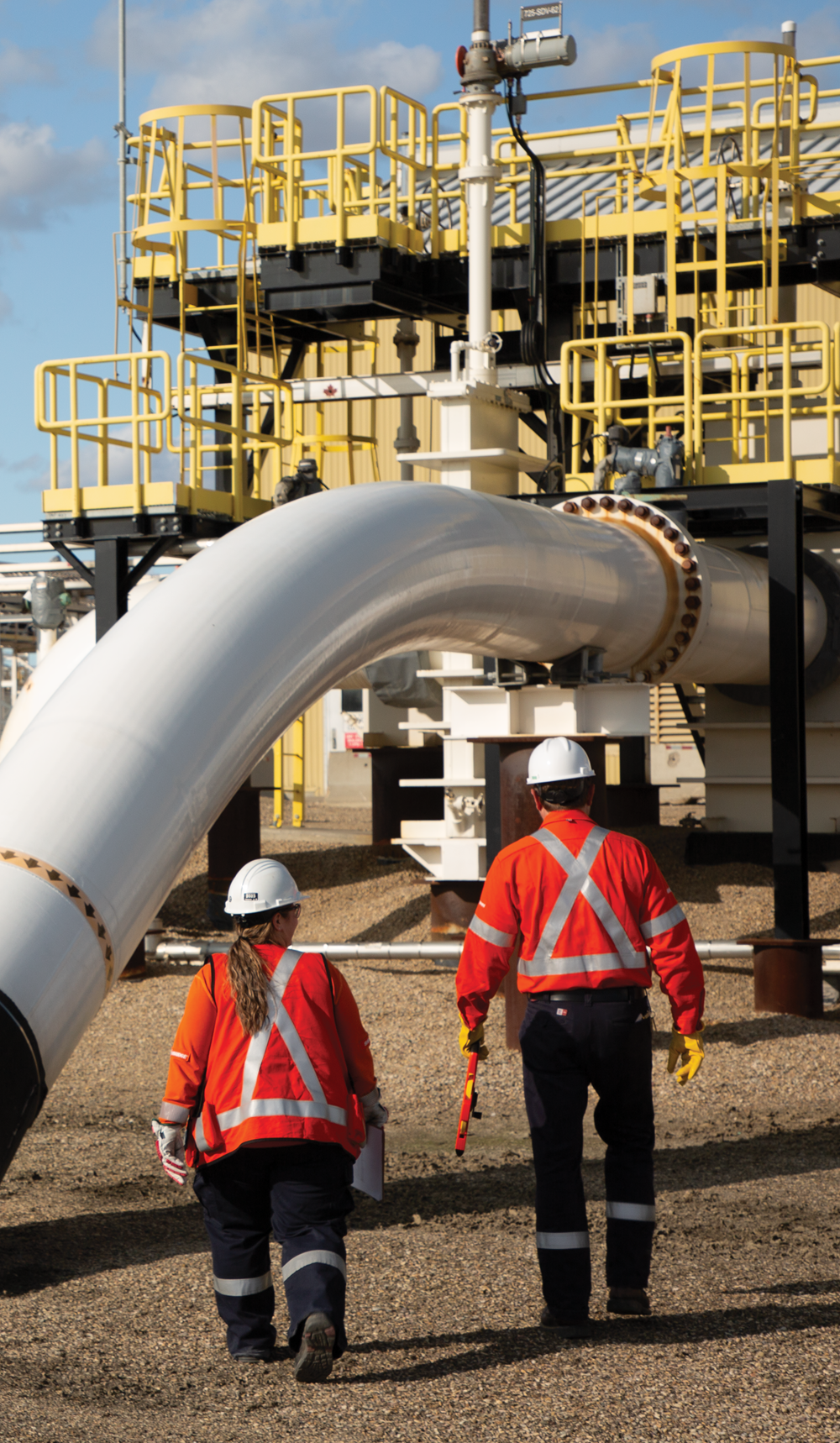 Two workers walking past large above-ground pipe