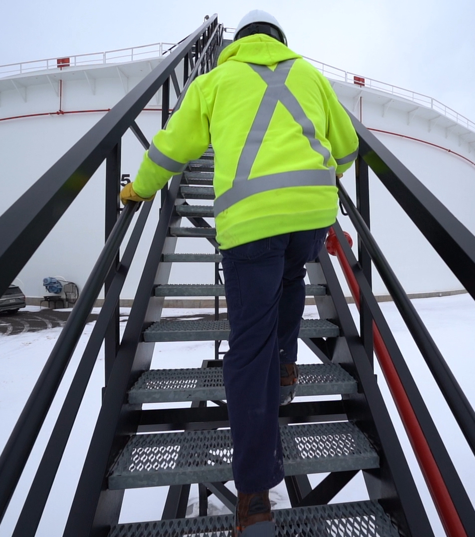 Worker climbing ladder to a tank