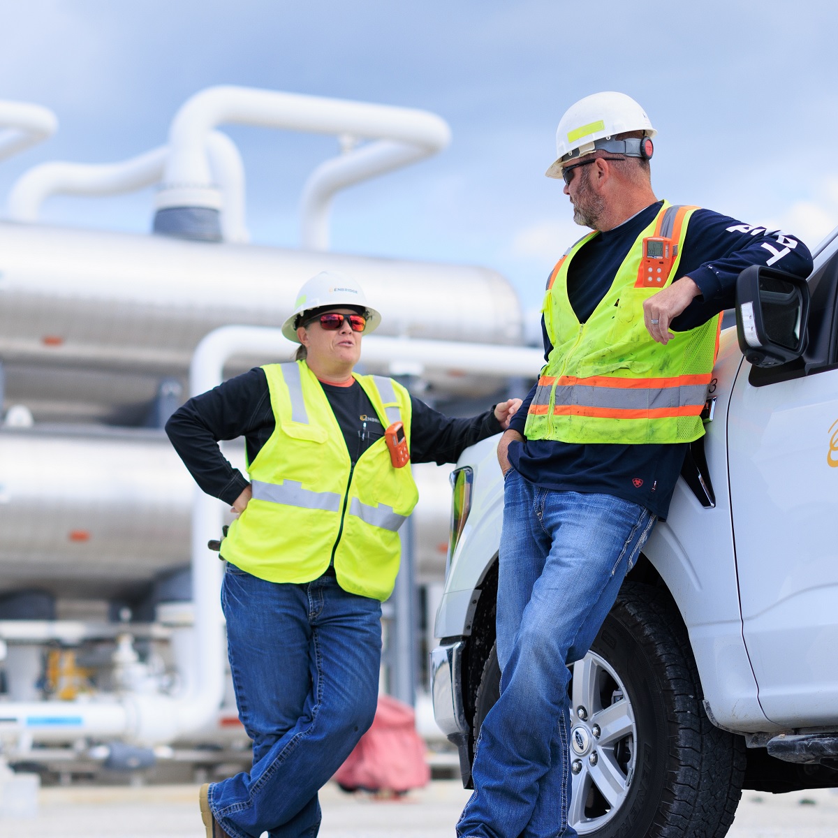 Two workers in safety gear at a piping facility