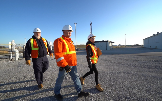Three people walking across a gravel parking lot at sunrise