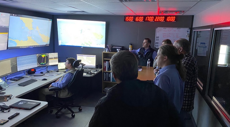 People watching an operator monitor screens at a control center