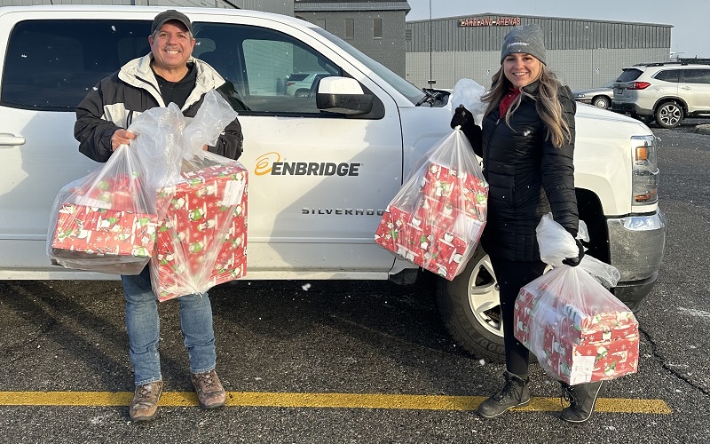 Two people standing with Christmas gifts to donate