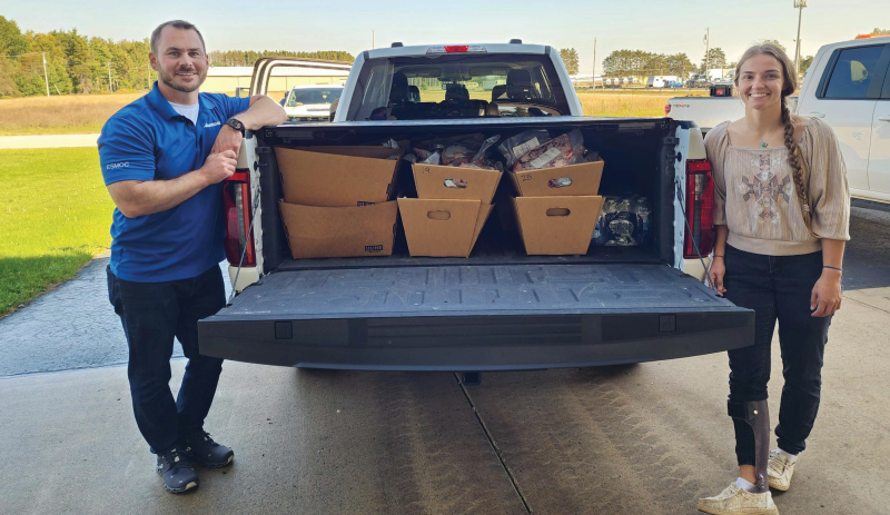 People standing beside the back of a truck filled with boxes of ground beef