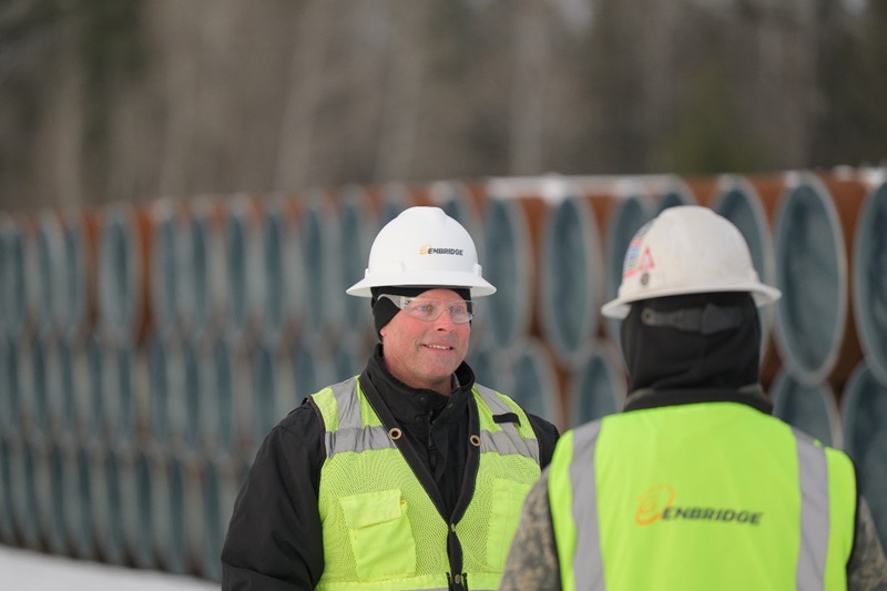 Construction workers in white helmets at a pipe yard