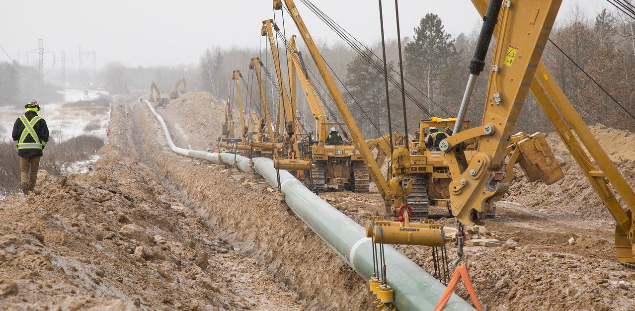 Cranes lowering a pipeline into a trench