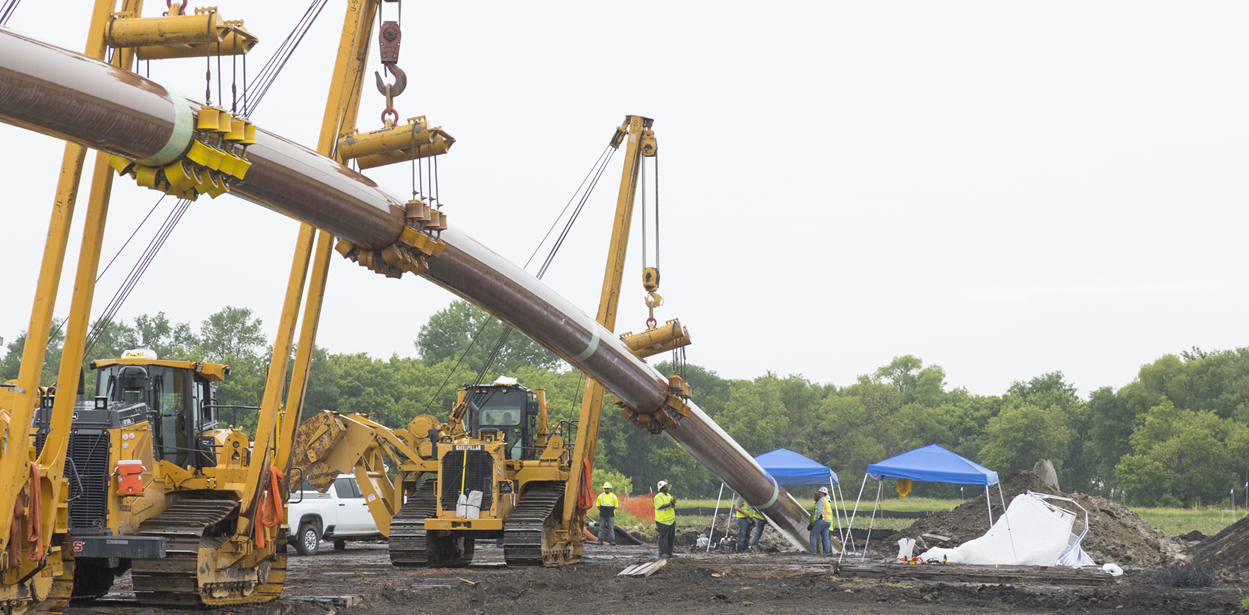 Large cranes holding up a long segment of pipe