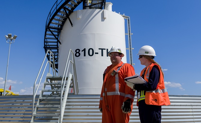 Two workers in front of a crude storage tank